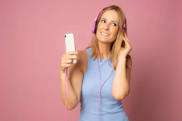 Young smiling woman joyful listening to music on mobile phone isolated over pink background.