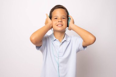 Sevimli, gülümseyen çocuk kulaklıklı ve baş parmaklı müziği beyaz arka planda izole bir şekilde dinle..