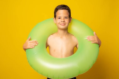 Sarı arka planda izole edilmiş bir yüzme yüzüğü tutan sevimli küçük çocuk.