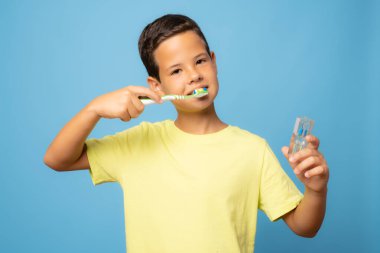 Mavi arka planda diş fırçası olan genç bir çocuk..