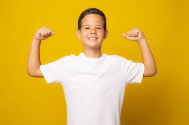 Güçlü çocuk kaslarını gösteriyor, sarı arka planda izole edilmiş.