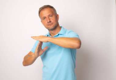 Beyaz arka planda mavi t-shirt giyen genç beyaz bir adam bir mola jesti göstererek üzgün