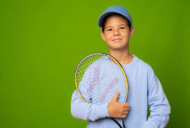 Yeşil arka planda izole edilmiş tenis raketiyle gururlu bir çocuk..