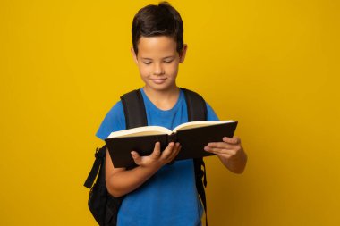 Sarı arka planda izole bir kitap tutan mutlu okul çocuğu..