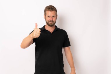 Beyaz arka planda izole edilmiş kameraya gülümseyen ve baş parmağını gösteren basit giysili neşeli bir adamın portresi.