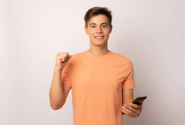Симпатичный Молодой Человек Мобильным Телефоном Делает Жест Победителя Белом Фоне — стоковое фото
