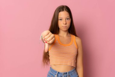 Genç ve güzel bir kız pembe arka planda duruyor mutsuz ve kızgın görünüyor. Reddedilmiş ve olumsuz..