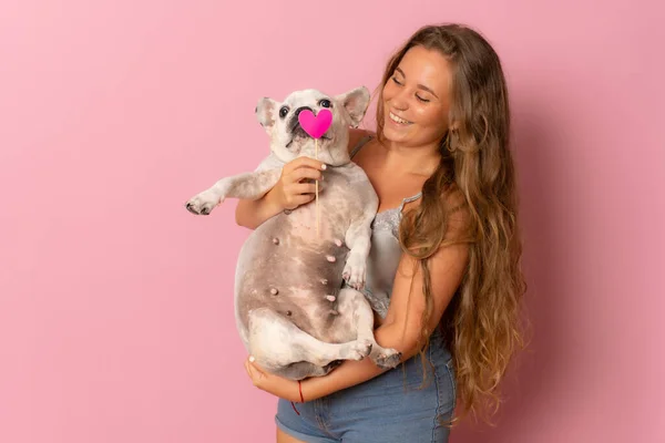 一个女孩抱着一只法国斗牛犬 与粉红的背景隔离在怀里 — 图库照片