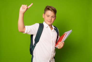 Okul çantalı ve parmakla işaret eden kitapları olan bir çocuk.