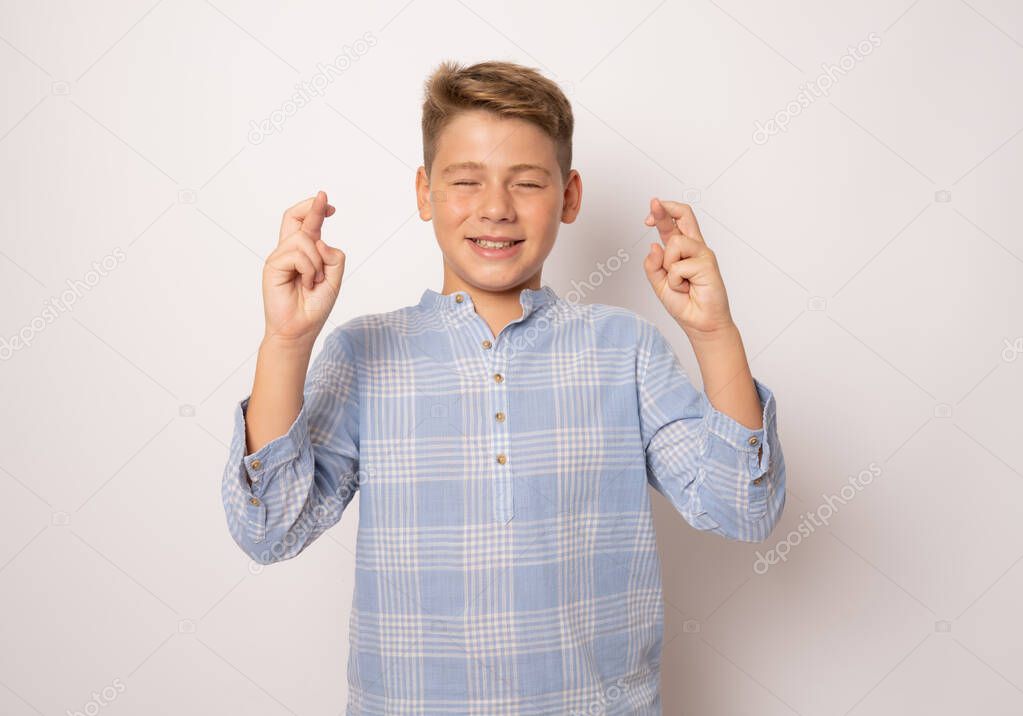 Young boy crossing fingers for having luck isolated over white background.
