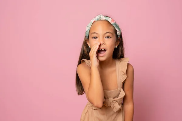 Küçük kızın gizli dedikoduları anlattığı fotoğraf portresi Pastel pembe arka planda sessizce izole edilmiş fotokopi alanı ile fısıldıyor.