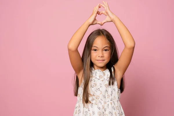 ポジティブな陽気な子供の女の子の肖像画は ハートの指の形をしますショー恋人サイン感情隔離されたピンクの背景 — ストック写真
