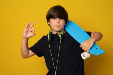 Sarı arka planda izole edilmiş kaykayı tutan genç havalı çocuk..