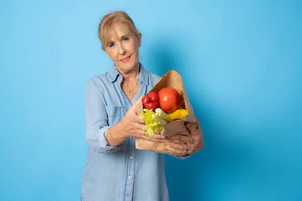 Senior shopping woman with grocery items. Isolated over blue background.
