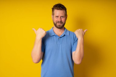 İzole edilmiş sarı arka planda genç yakışıklı adam işaret işareti gösteriyor.