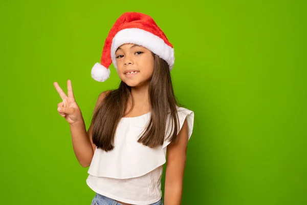 Happy Little Girl Kapeluszu Santa Gestem Znak Zwycięstwa Nad Zielonym — Zdjęcie stockowe