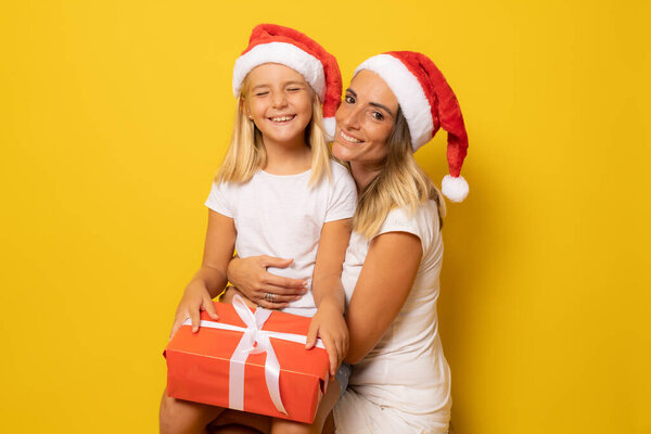 Happy mother and daughter in santa hat over yellow background. Christmas season concept.