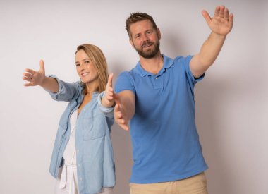 Beyaz arka planda poz veren genç bir çift kameraya sarılıyor..