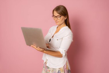 Pembe arka planda dizüstü bilgisayar kullanarak izole edilmiş güzel bir genç kadın görüntüsü.