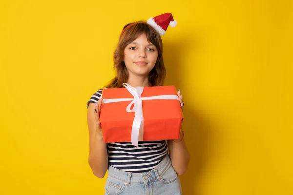 Lächelndes Junges Mädchen Mit Weihnachtsmannmütze Hält Geschenkbox Isoliert Über Gelbem — Stockfoto