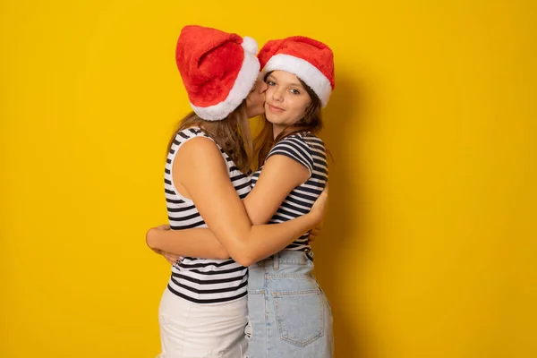 Mãe Beijando Sua Filha Chapéu Papai Noel Sobre Fundo Amarelo — Fotografia de Stock