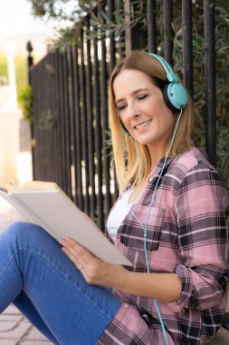 Gündelik gömlekli ve gözlüklü güzel bir kadın yeşil yaz parkına karşı beyaz kitap okuyor..