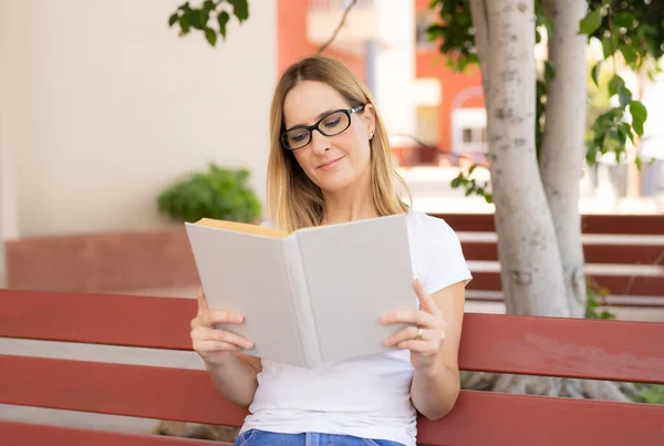 若い女性が公園のベンチに座って本を読んで — ストック写真