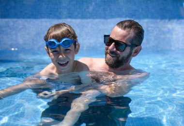 Neşeli bir baba ve küçük oğlu güneşli bir yaz gününde havuzda eğleniyorlar. Tatil kavramı.
