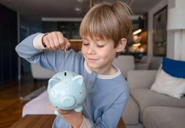 Pijamalı küçük sarışın bir çocuğun portresi. Kumbarayı alıp para biriktirmek için para koyuyor.