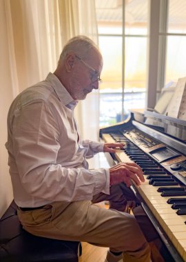 Yaşlı gri saçlı adam evde piyano çalıyor..
