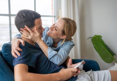 Genç ve gülümseyen bir annenin portresi. Evinde küçük oğluna sarılıyor. Aile bağları.