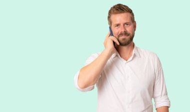 Beyaz gömlekli genç iş adamı yeşil arka planda cep telefonuyla konuşuyor. Boşluğu kopyala.