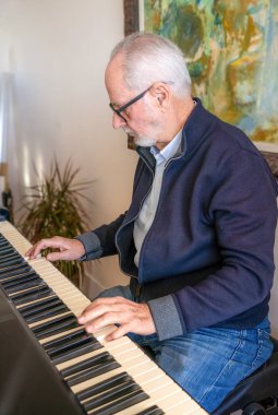 Kıdemli beyaz saçlı adam evde piyano çalıyor..