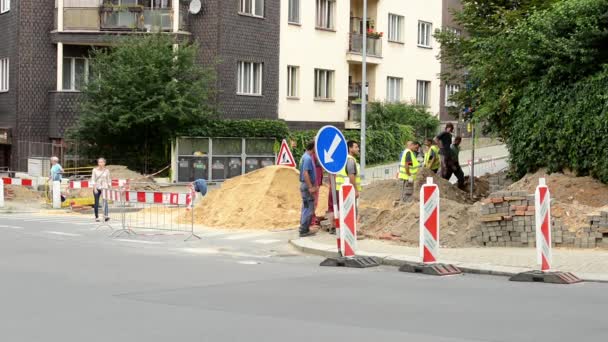 Reparere tettstedsgate med bebyggelse - med arbeidere - kvinne som går – stockvideo