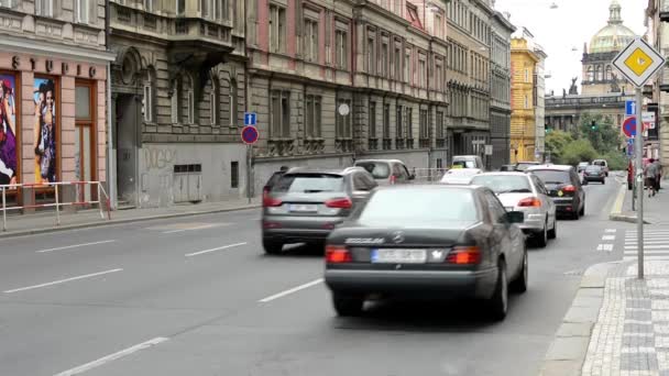 Urban street med forbipasserende biler: folk gå på fortovet bygninger i byen i baggrunden – Stock-video