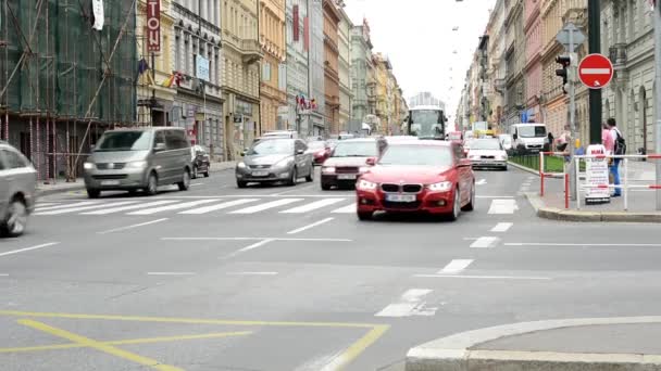 Urban street with passing cars and pedestrian crossing: people walking - buildings in the city in background — Stock Video