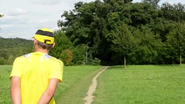 Мужской спорт - бег - мужчина разогревается перед бегом - парк (деревья и трава) - облачное небо - слайдер — стоковое видео