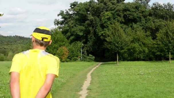 Deportes de hombre - correr - hombre calentando antes de correr - parque (árboles y hierba) - cielo nublado - deslizador — Vídeo de stock