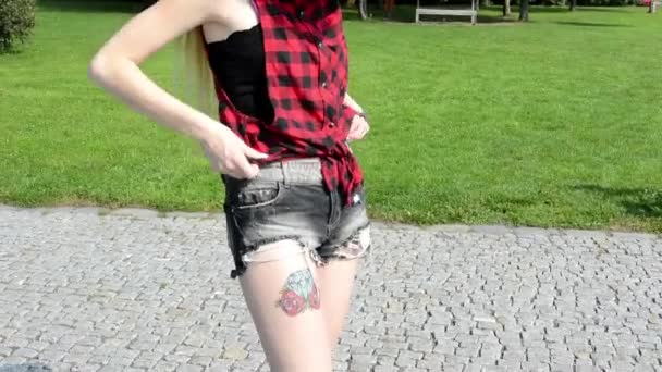 Mujer atractiva joven está en el parque - naturaleza - mujer ajusta la ropa, saca y mira el teléfono inteligente - tatuaje en el cuerpo - naturaleza — Vídeo de stock