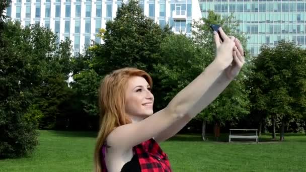 Ung attraktiv kvinna i park - kvinna fotograferar själv (selfie) - natur och moderna byggnader — Stockvideo