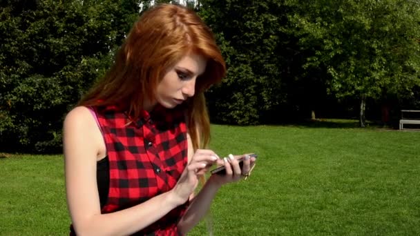 Young attractive woman is in the park - woman works on the smartphone (sms) - nature - she has serious expression — Stock Video