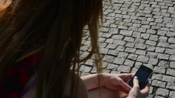 Jeune femme séduisante assis sur bech dans le parc - femme travaille sur le smartphone (sms) - trottoir (pavé) en arrière-plan — Video