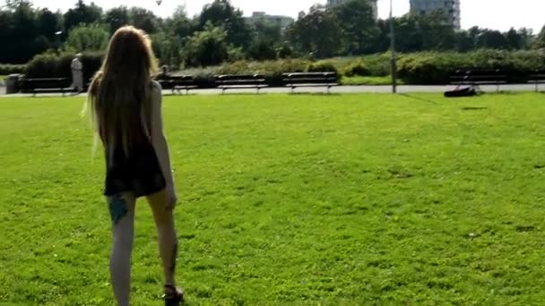 Mujer atractiva joven (tatuaje) va en el parque - naturaleza con edificios modernos en el fondo — Vídeos de Stock