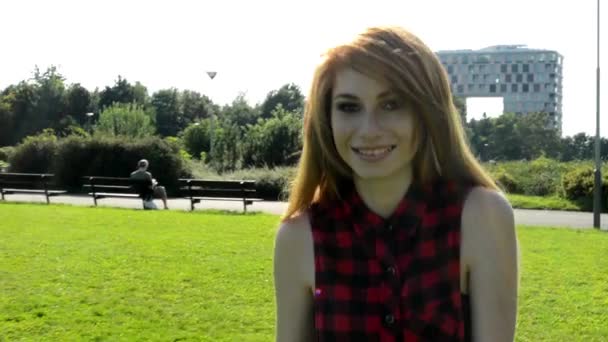 Young attractive woman goes in park and smiles - nature with modern buildings in background — Stock Video