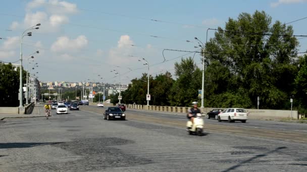 Strada urbana con auto di passaggio - edifici sullo sfondo - natura (alberi) - persone - cielo nuvoloso (soleggiato ) — Video Stock