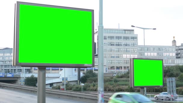 Два билборда в городе у дороги - зеленый экран - здание и проезжающие машины на заднем плане — стоковое видео