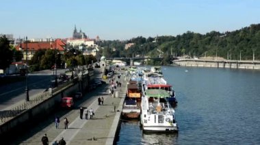 İskele (Vltava) - arka plan - Prag Kalesi (Hradcany) - güneşli (mavi gökyüzü) - otomobil ve ağaçlar - yürüme şehir (bina) Nehri üzerinde tekne insanlar - waterfront