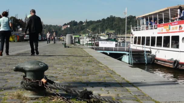 Barcos en el río en muelle (Vltava) - ciudad (edificios y árboles) en el fondo - personas caminando - frente al mar - soleado (cielo azul ) — Vídeos de Stock