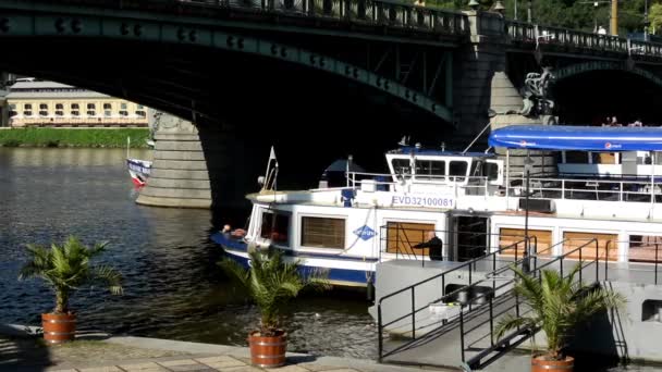 Hajók a folyó - híd - autók és a fák - emberek gyaloglás - waterfront quay (Vltava) - napos (kék ég) — Stock videók