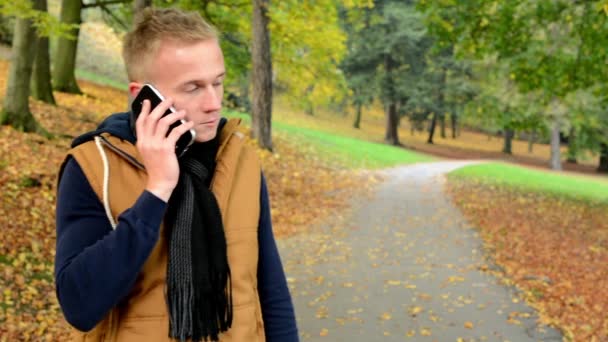 Man op de telefoon (man die door smartphone) - man glimlach (gelukkig) - man in de herfst park (aard) — Stockvideo